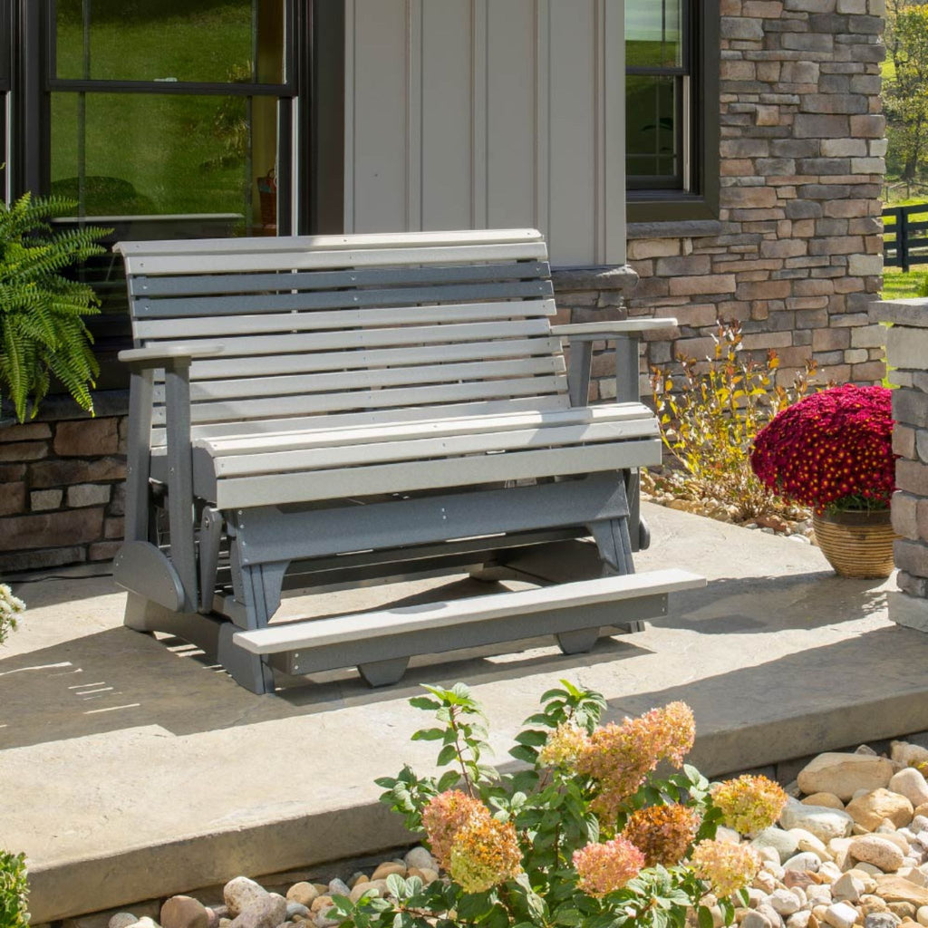 Gray wooden bench on a patio with flowers and a stone wall in the background