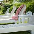 White outdoor lounge chairs with a pink blanket and bottles on a grassy area