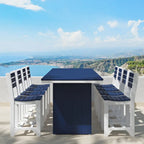 A 5-piece outdoor bar-height dining set with a square table and four matching high-back chairs, featuring white frames and dark navy cushions, set against a scenic coastal background.