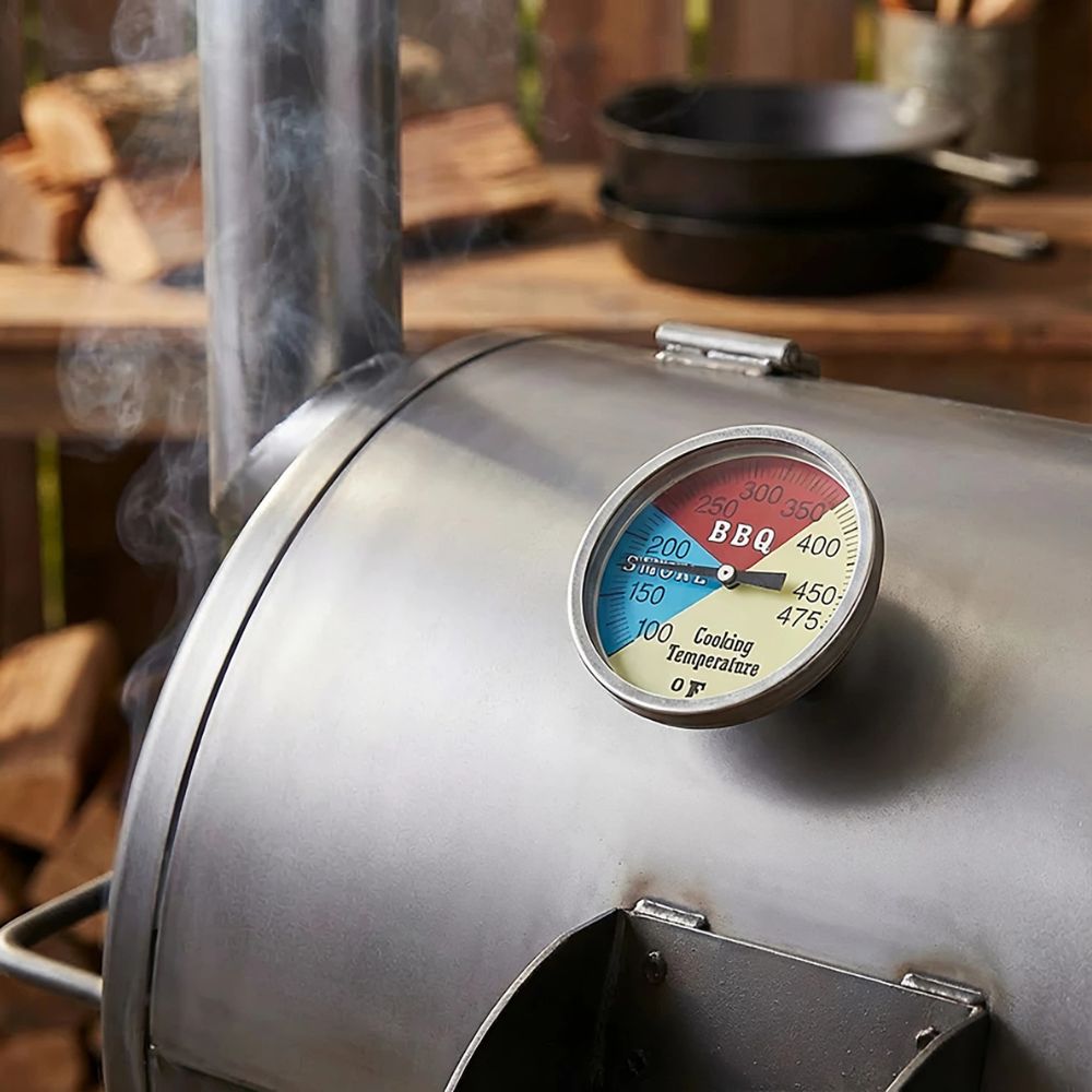 Metallic BBQ smoker with a thermometer on a wooden background