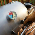 Grill with a thermometer and gloved hand adjusting it on a wooden deck.