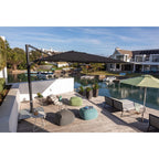 Outdoor patio scene with a large black cantilever umbrella over lounge chairs and bean bags, next to a green patio umbrella by the water, with houses and boats in the background.