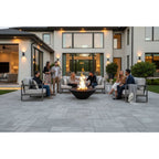 Group of people gathered around a fire pit on a patio in front of a modern house.