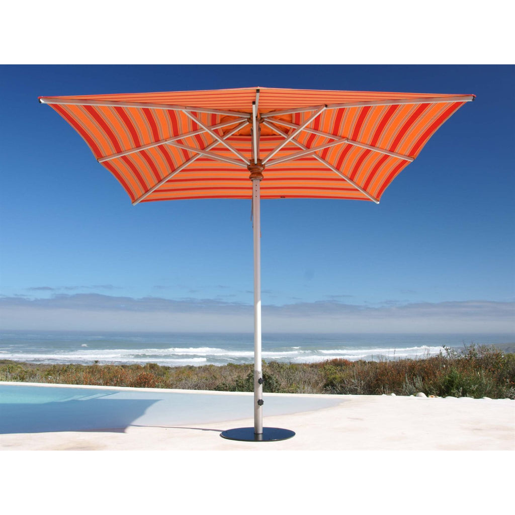 An orange and red striped patio umbrella with a silver metal pole, positioned next to a swimming pool with a beach and ocean view in the background.
