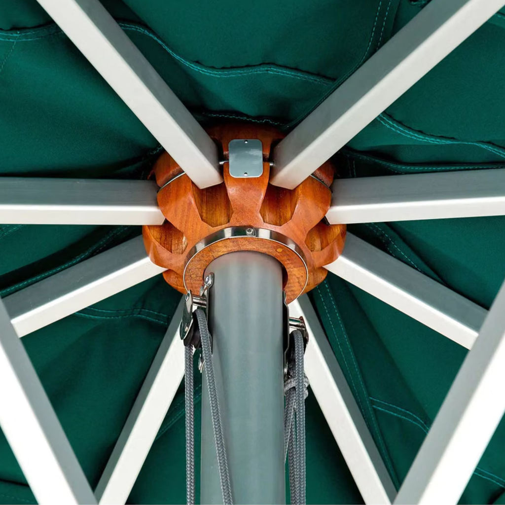 Close-up of a patio umbrella canopy and frame, showing a dark teal fabric canopy, white metal ribs, a gray central pole, and an orange-brown wooden central cap.