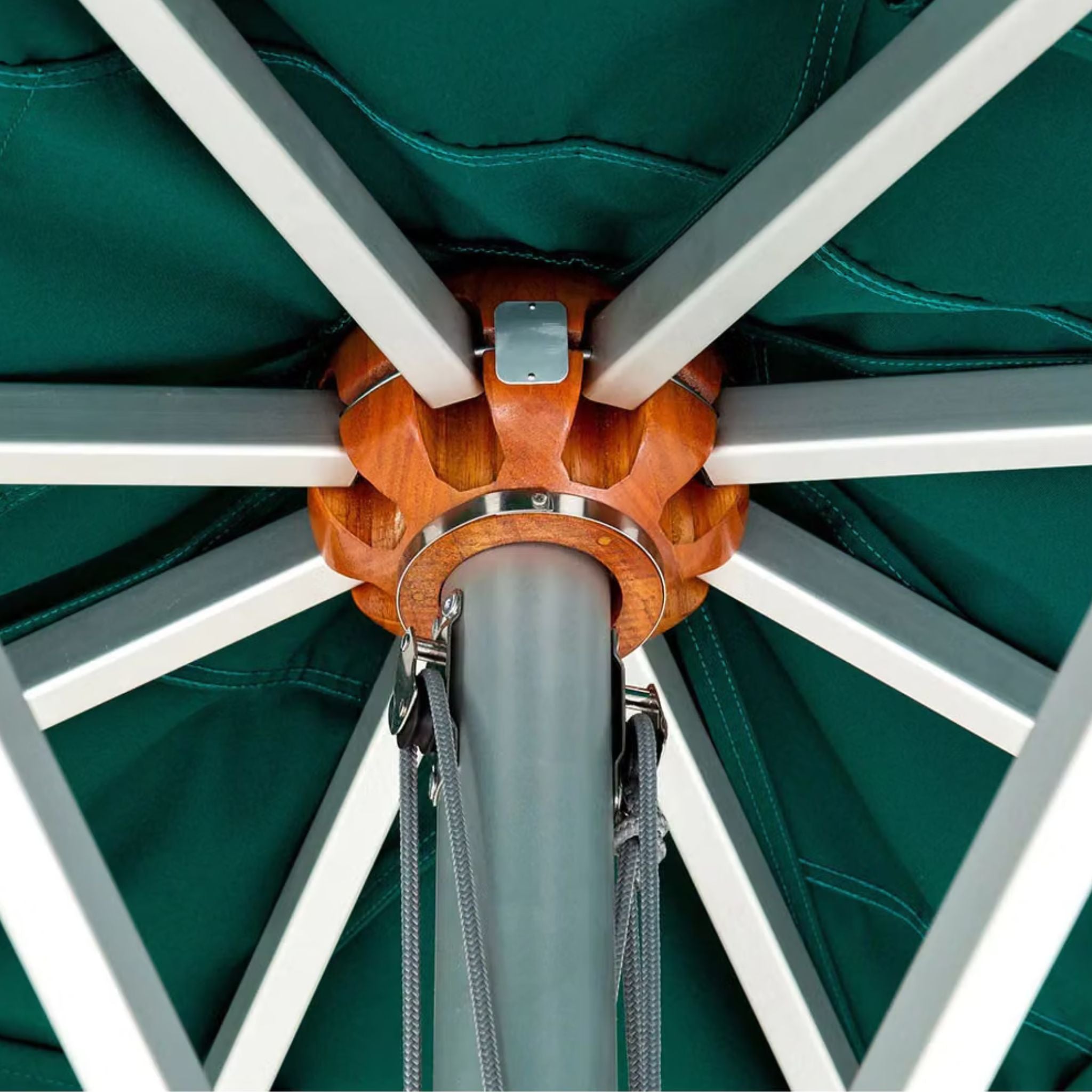 Close-up of a patio umbrella canopy and frame, showing a dark teal fabric canopy, white metal ribs, a gray central pole, and an orange-brown wooden central cap.