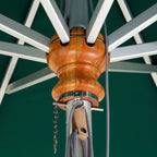 Close-up of a wooden umbrella pull ring and canopy attachment hardware on a green patio umbrella, showing the warm brown wood grain, silver metal bands, and gray cords.