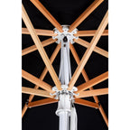 Close-up of a patio umbrella canopy and frame, showing a black fabric canopy, natural wood ribs, and a white central pole and hardware.