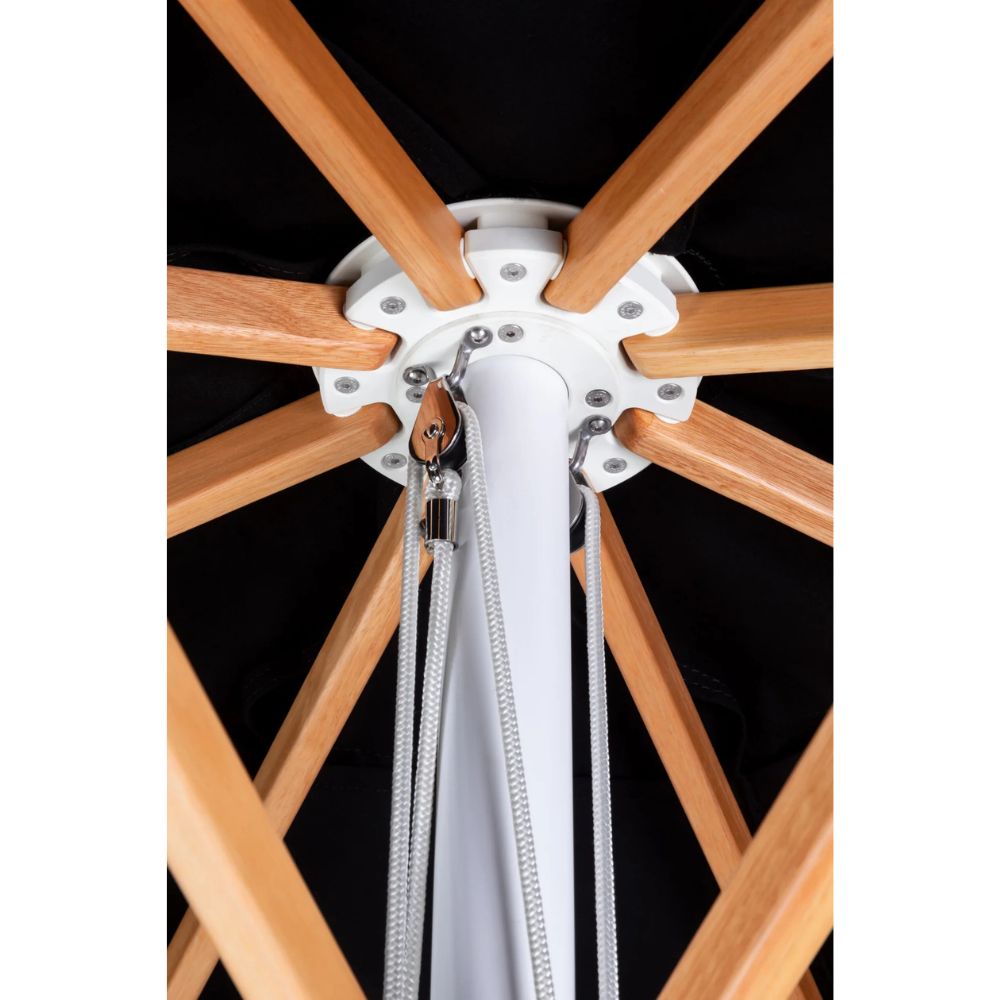 Close-up detail of an umbrella frame showing the central white hub, natural wood radial ribs, and white hanging cords against a black canopy background.