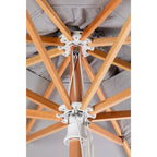 Close-up of the underside of a patio umbrella showing light natural wood ribs, white metal hardware, and a gray fabric canopy.