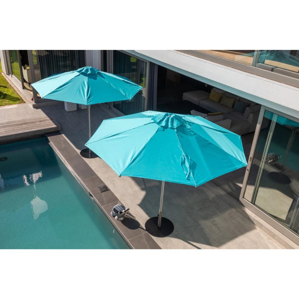 Two turquoise patio umbrellas on a modern outdoor deck beside a swimming pool, with a house interior visible in the background.