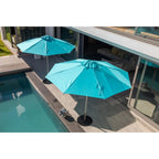 Two turquoise patio umbrellas on a modern outdoor deck beside a swimming pool, with a house interior visible in the background.